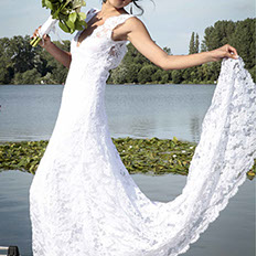 LA MARI2E EST EN POSE LAT2RALE AVEC UN BOUQUET DANS SA MAIN DROITE ET SA ROBE REHAUSS2E PAR SA MAIN GAUCHE SUR UN EMBARQUADERE