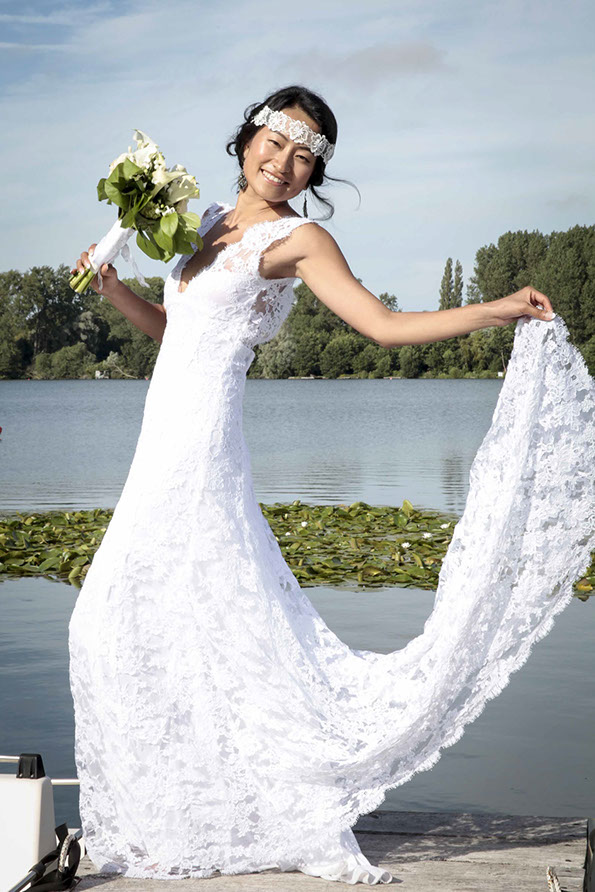 LA MARI2E EST EN POSE LAT2RALE AVEC UN BOUQUET DANS SA MAIN DROITE ET SA ROBE REHAUSS2E PAR SA MAIN GAUCHE SUR UN EMBARQUADERE