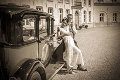 la mariée est accoudé sur la voiture ancienne et sonj marie est à ses cotés